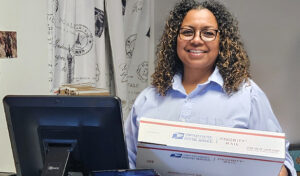 A smiling U.S. Postal Service worker processes a Priority Mail package at a Post Office